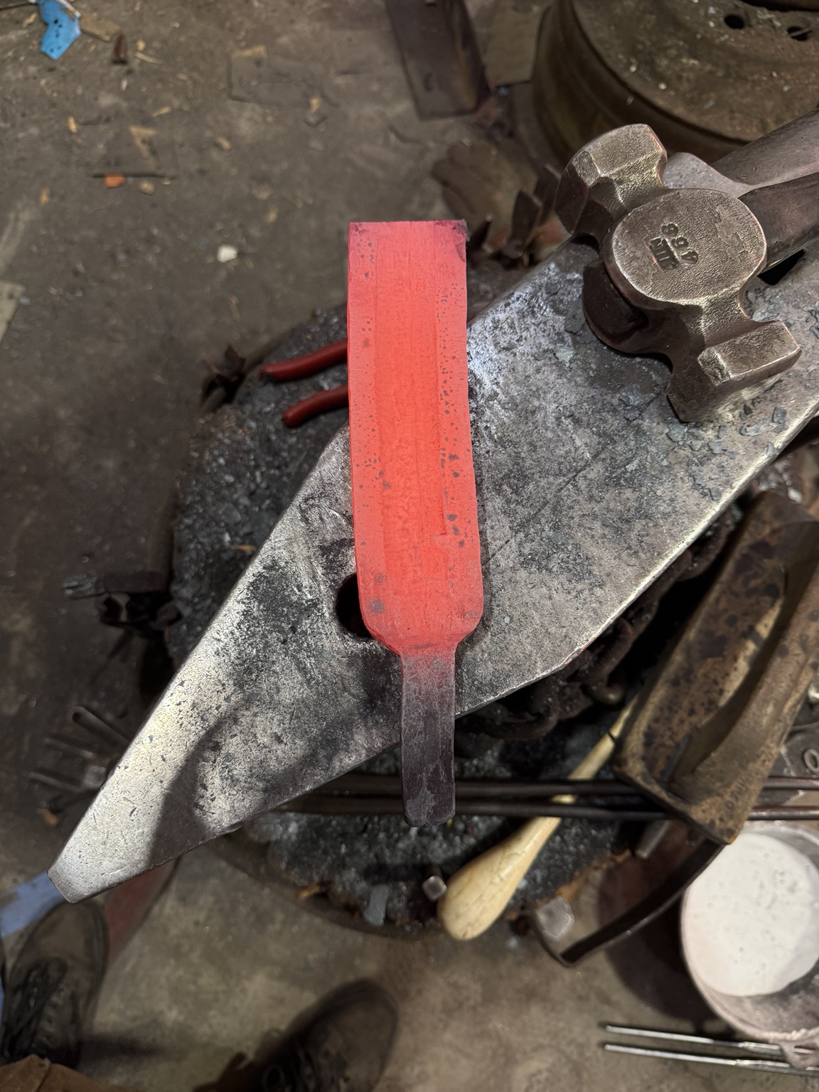 The rectangular composite billet glowing red hot on the anvil after forge welding