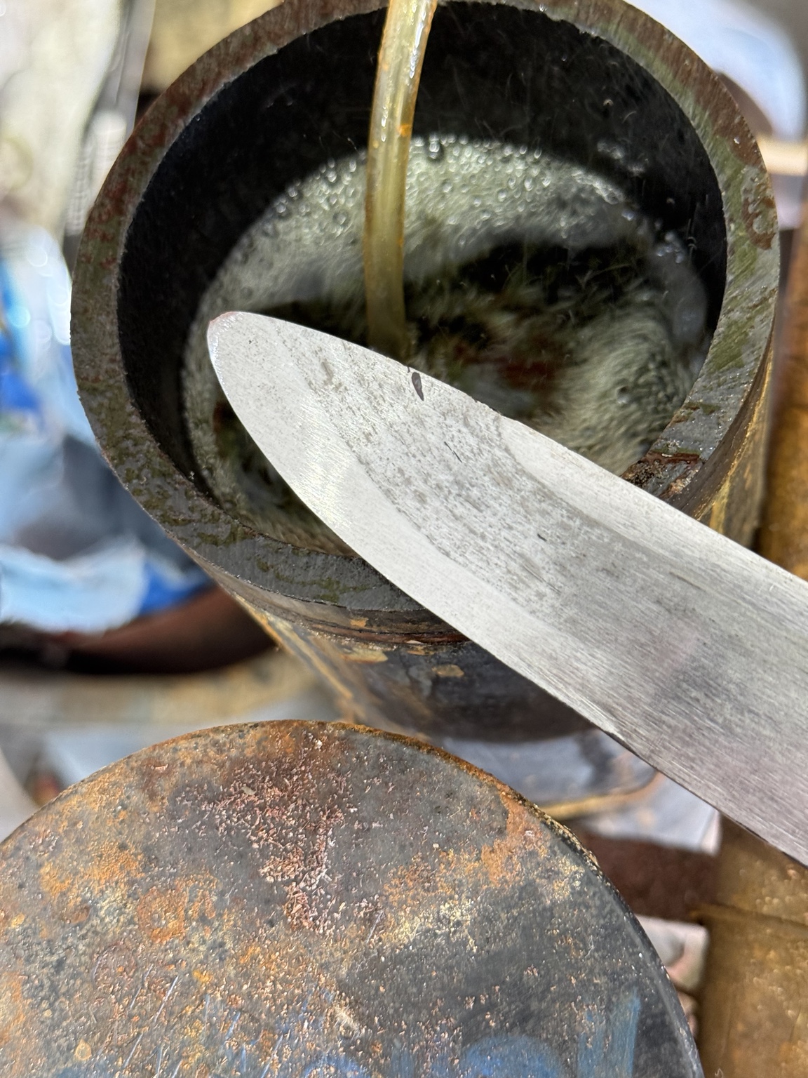 Reworked single-edged long knife blade point photographed beside a container in the forge
