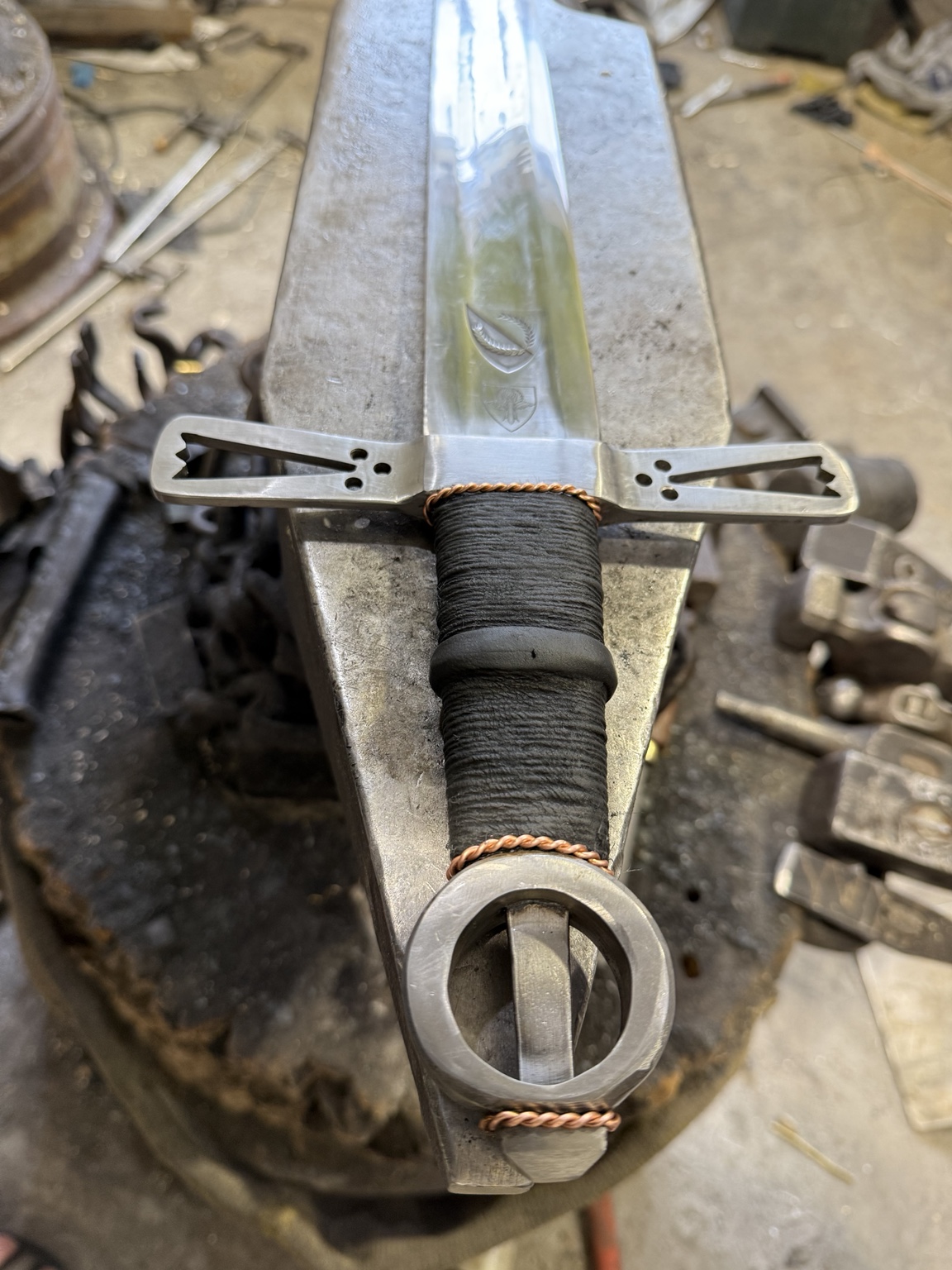 Detail of mild-steel ring pommel and black deerhide-wrapped grip resting on an anvil
