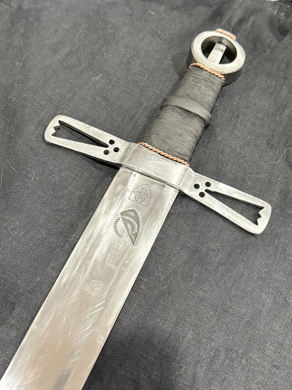 Detail of engraved heraldic devices, hand-filed steel crossguard and black leather grip
