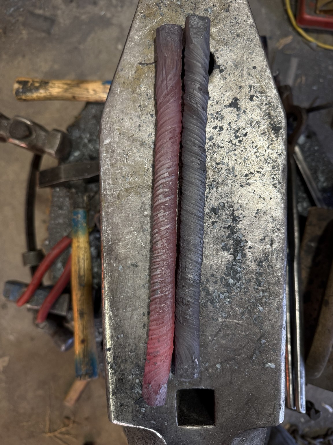 Two nine-layer twisted steel bars lying side by side on an anvil
