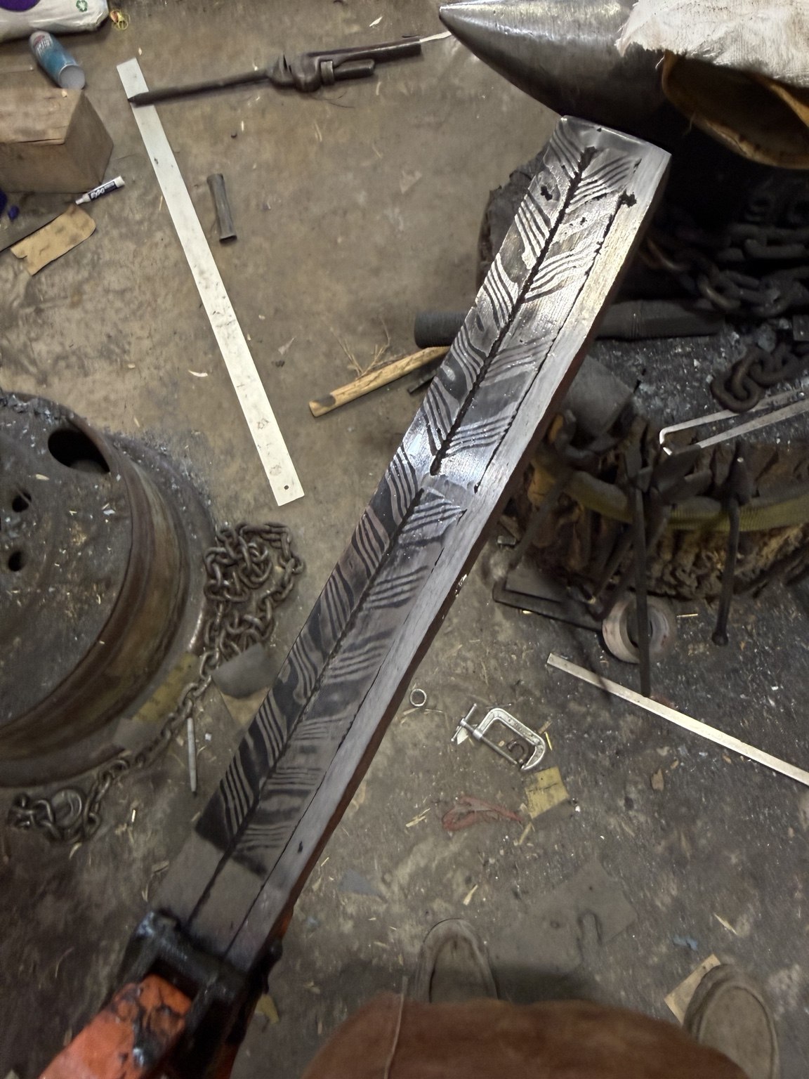 Long etched composite billet displaying a herringbone pattern and wrought-iron spine