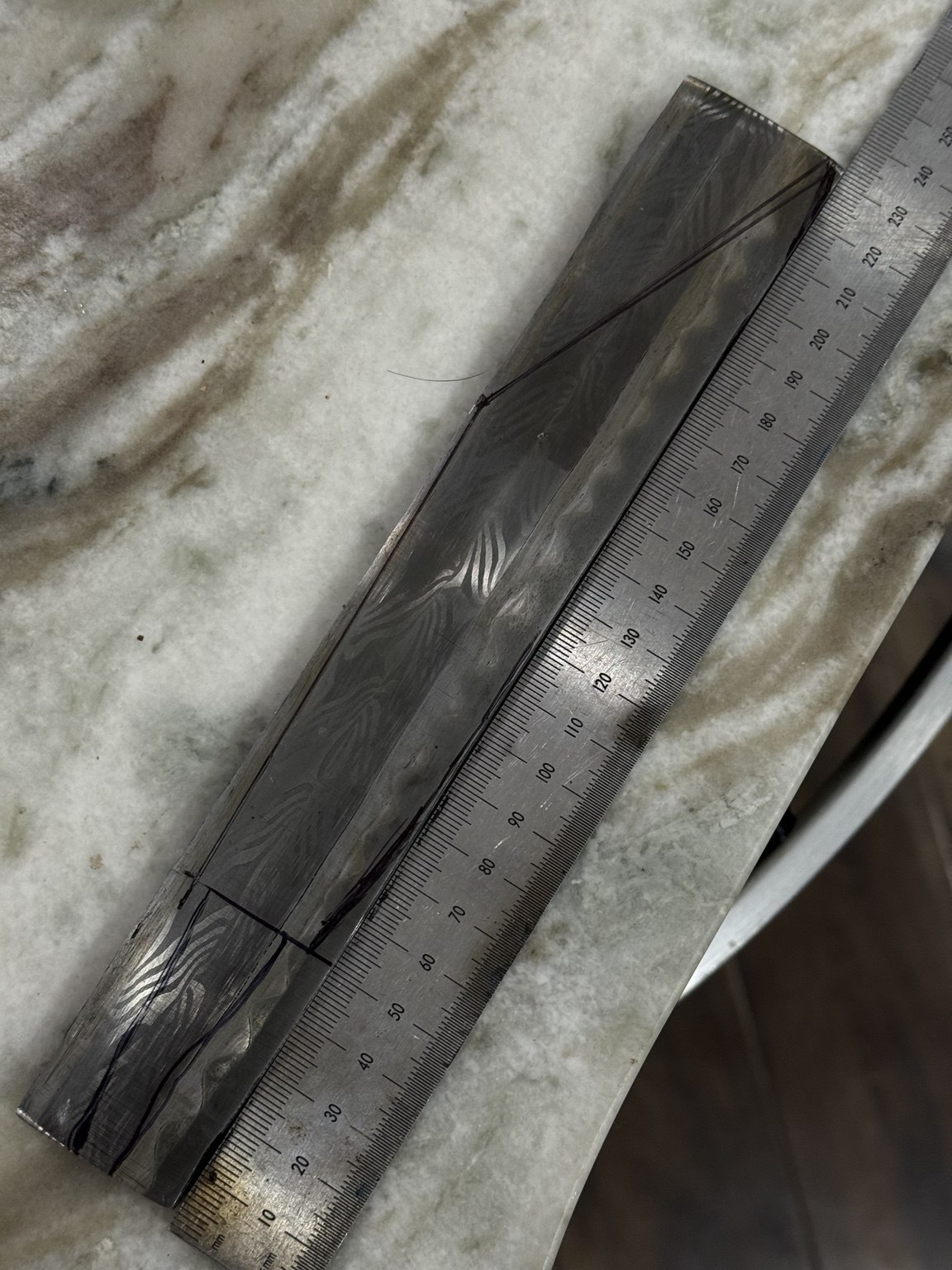 Etched composite billet with a blade outline drawn on it beside a metric ruler